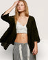Woman wearing a black jacket over a white lace top and striped pants on a plain background