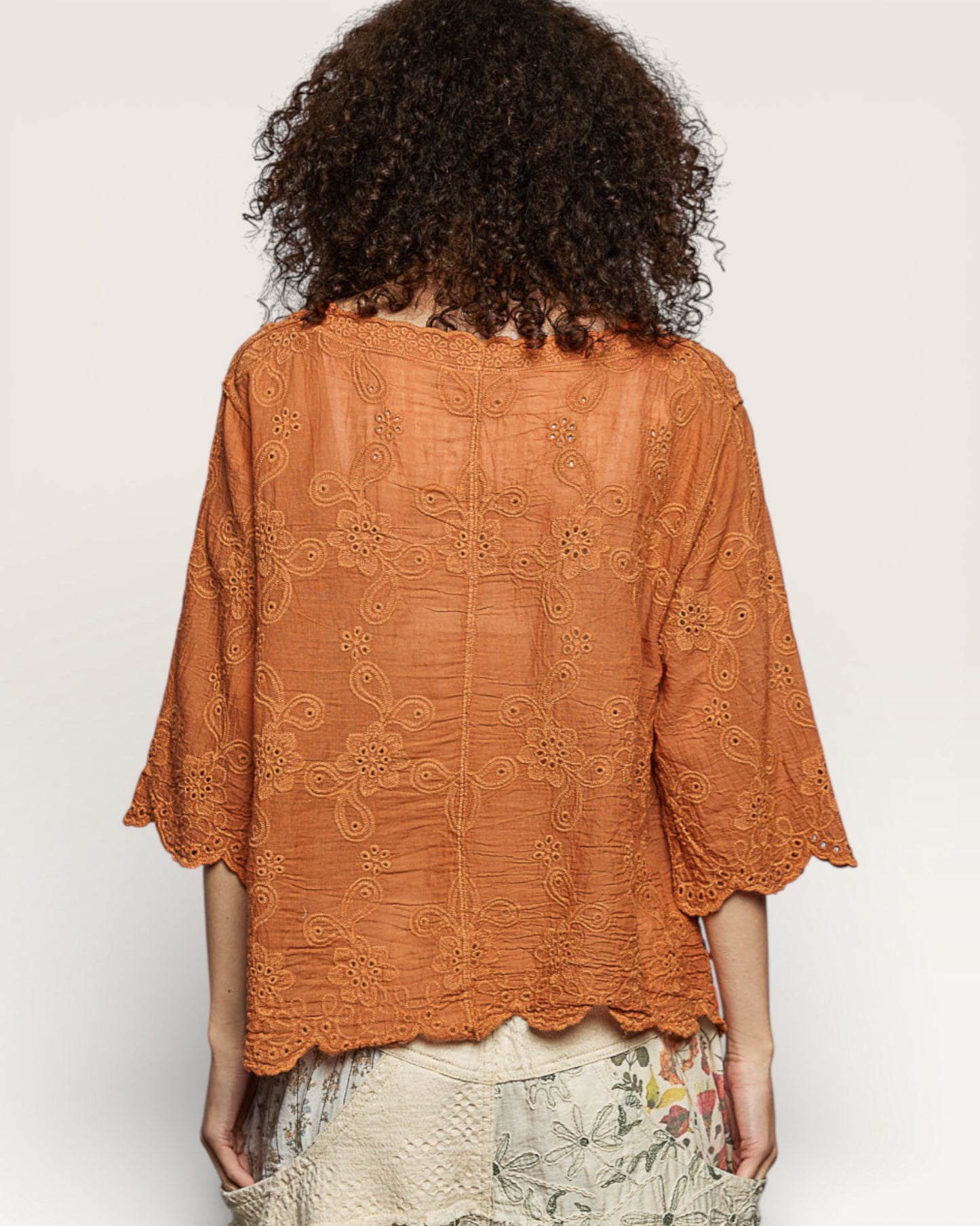 Person wearing an orange lace top on a plain background