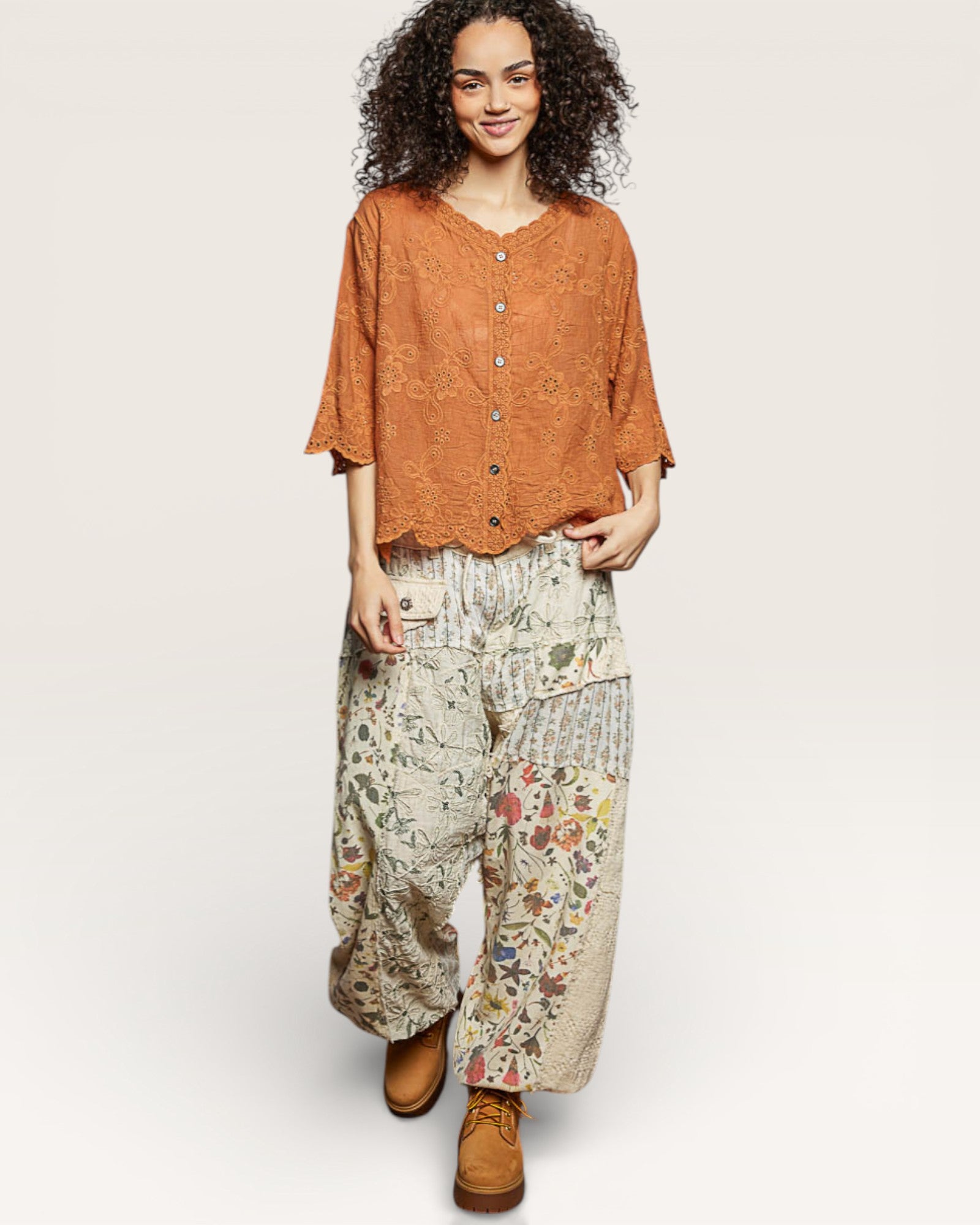 Woman wearing a rust-colored top and floral pants on a white background
