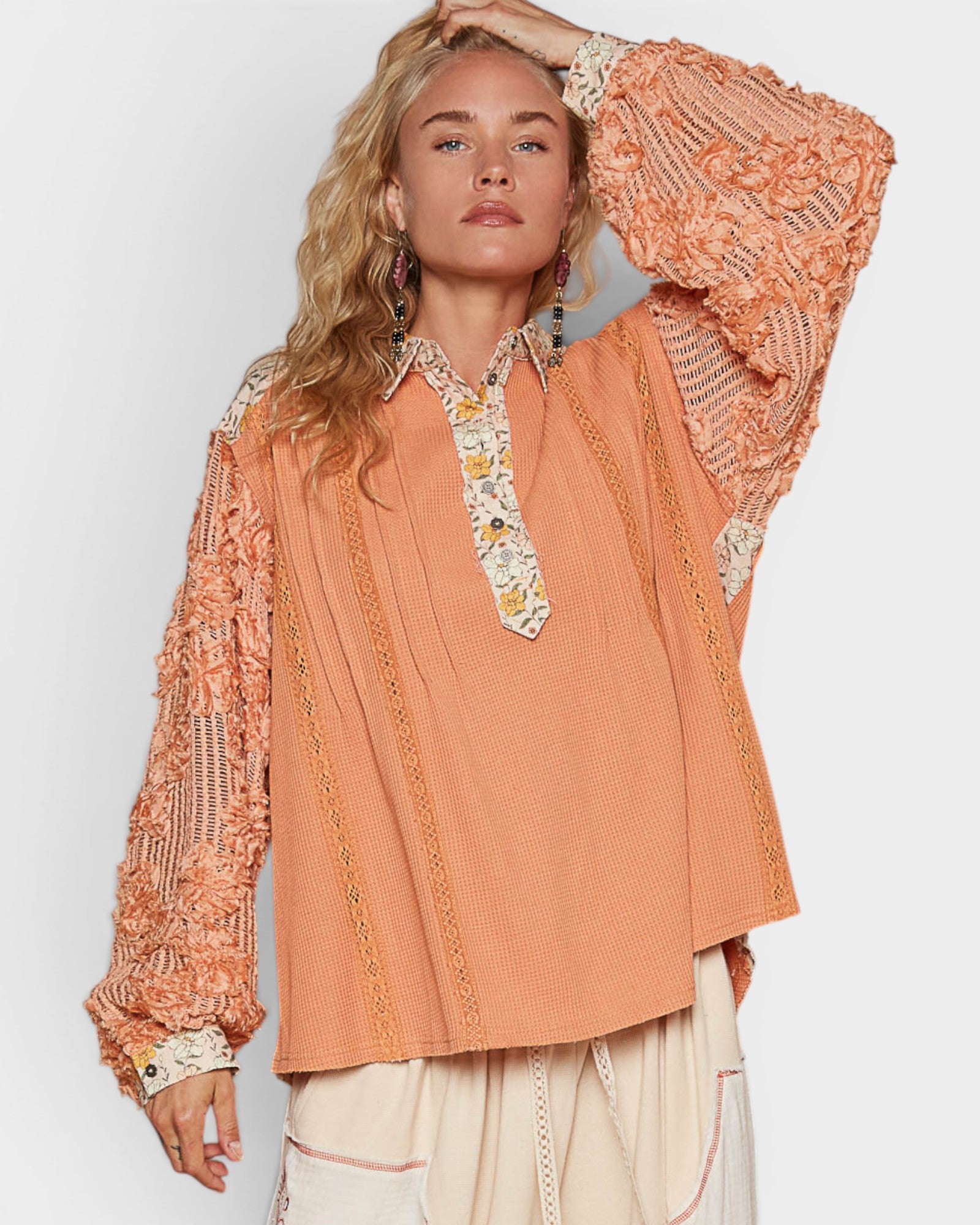 Woman wearing a peach-colored blouse with intricate lace details on a plain background