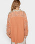 Coral blouse with lace details on a plain background