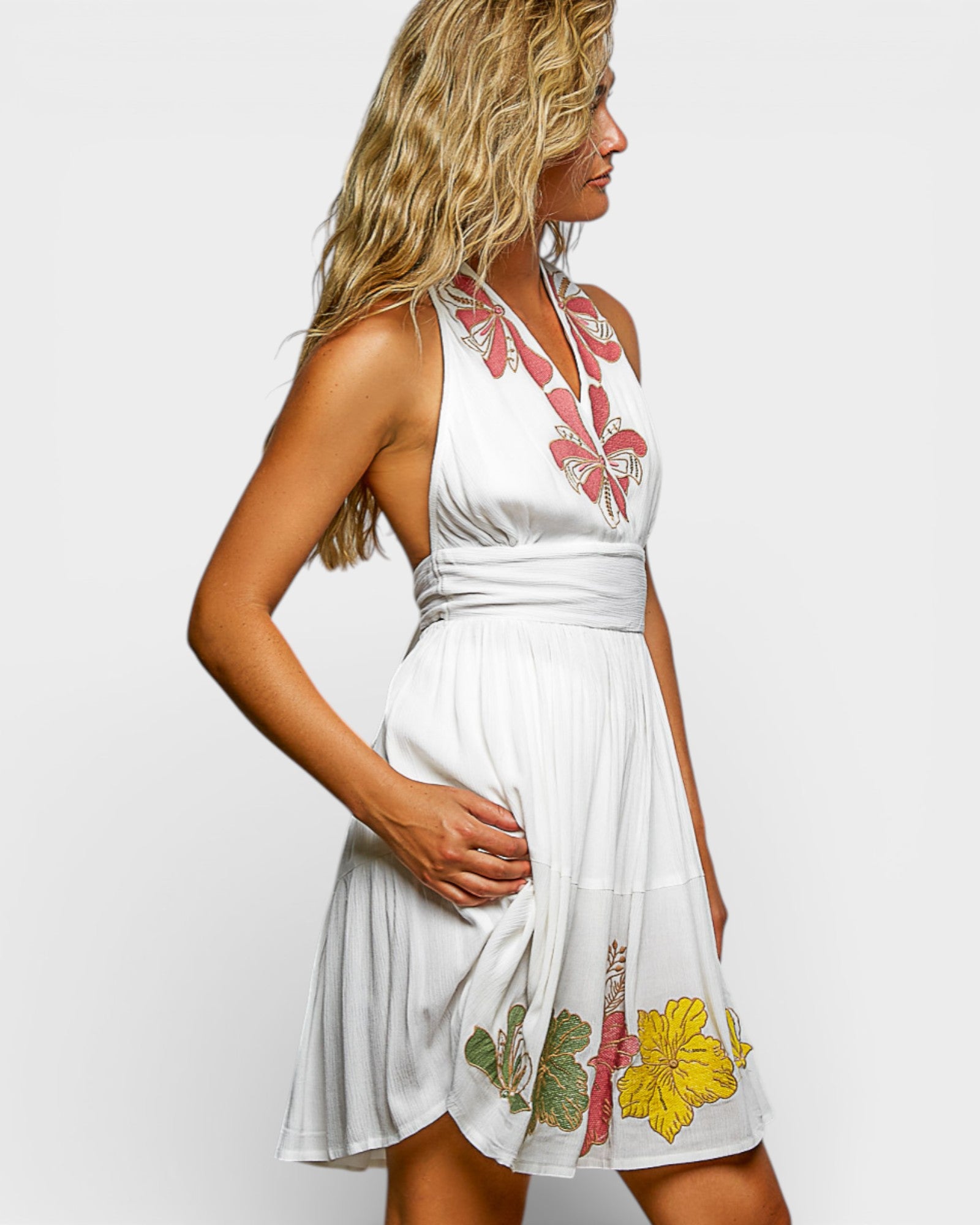 Woman wearing a white dress with floral embroidery on a plain background