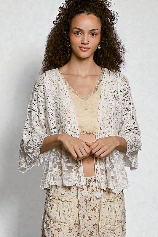 Woman wearing a white lace top and floral pants against a plain background