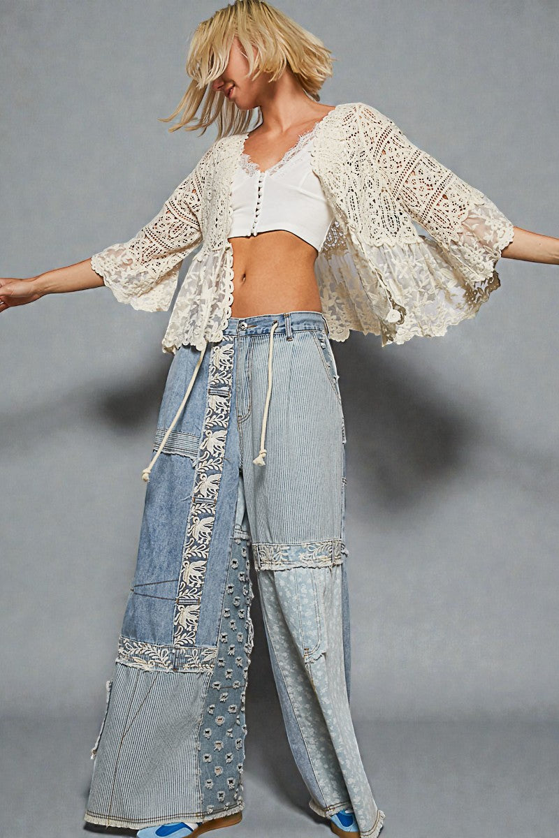 Person wearing a lace top and patchwork jeans on a gray background