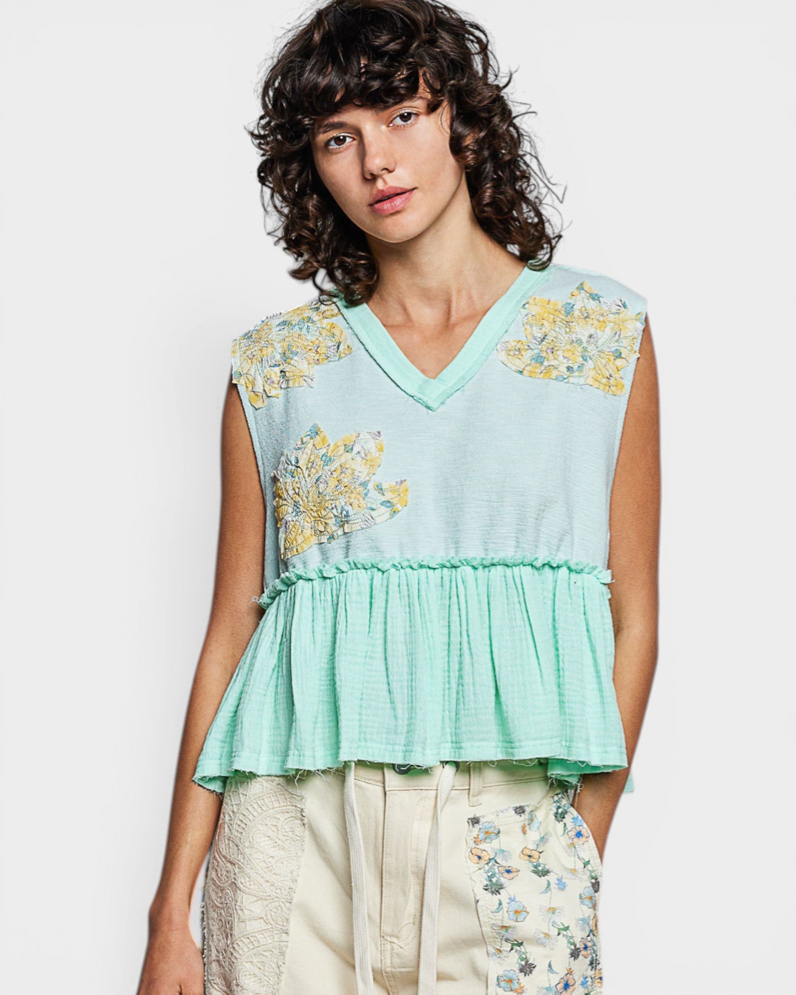 Woman wearing a light blue sleeveless top with floral embroidery on a white background