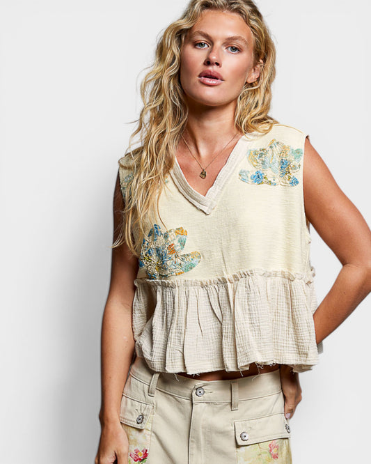 Woman wearing a floral embroidered top and beige pants against a white background