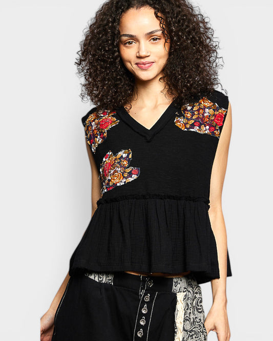 Woman wearing a black sleeveless top with floral patterns on a plain background