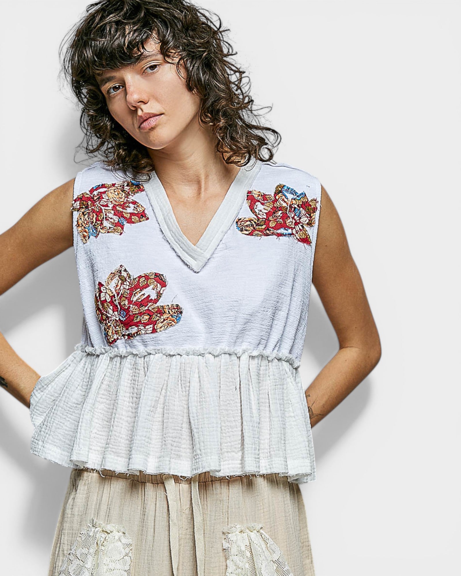 Woman wearing a sleeveless top with floral embroidery on a plain background