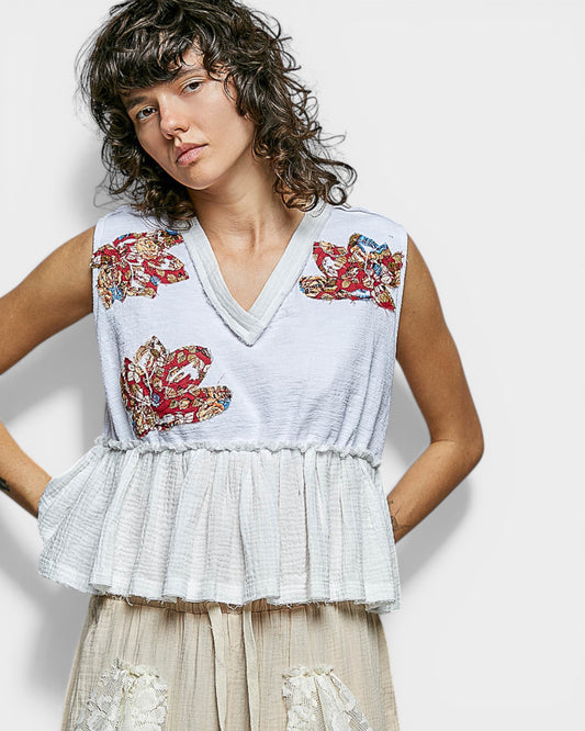 Woman wearing a sleeveless top with floral embroidery on a plain background