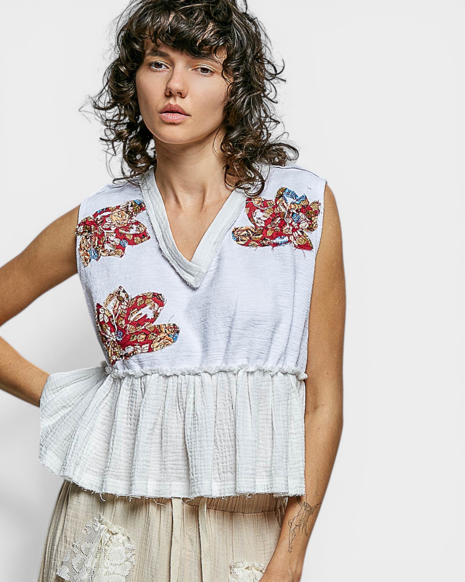 Woman wearing a sleeveless top with floral embroidery on a plain background