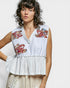 Woman wearing a sleeveless top with floral embroidery on a plain background