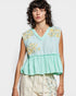 Woman wearing a light blue sleeveless top with floral embroidery on a white background