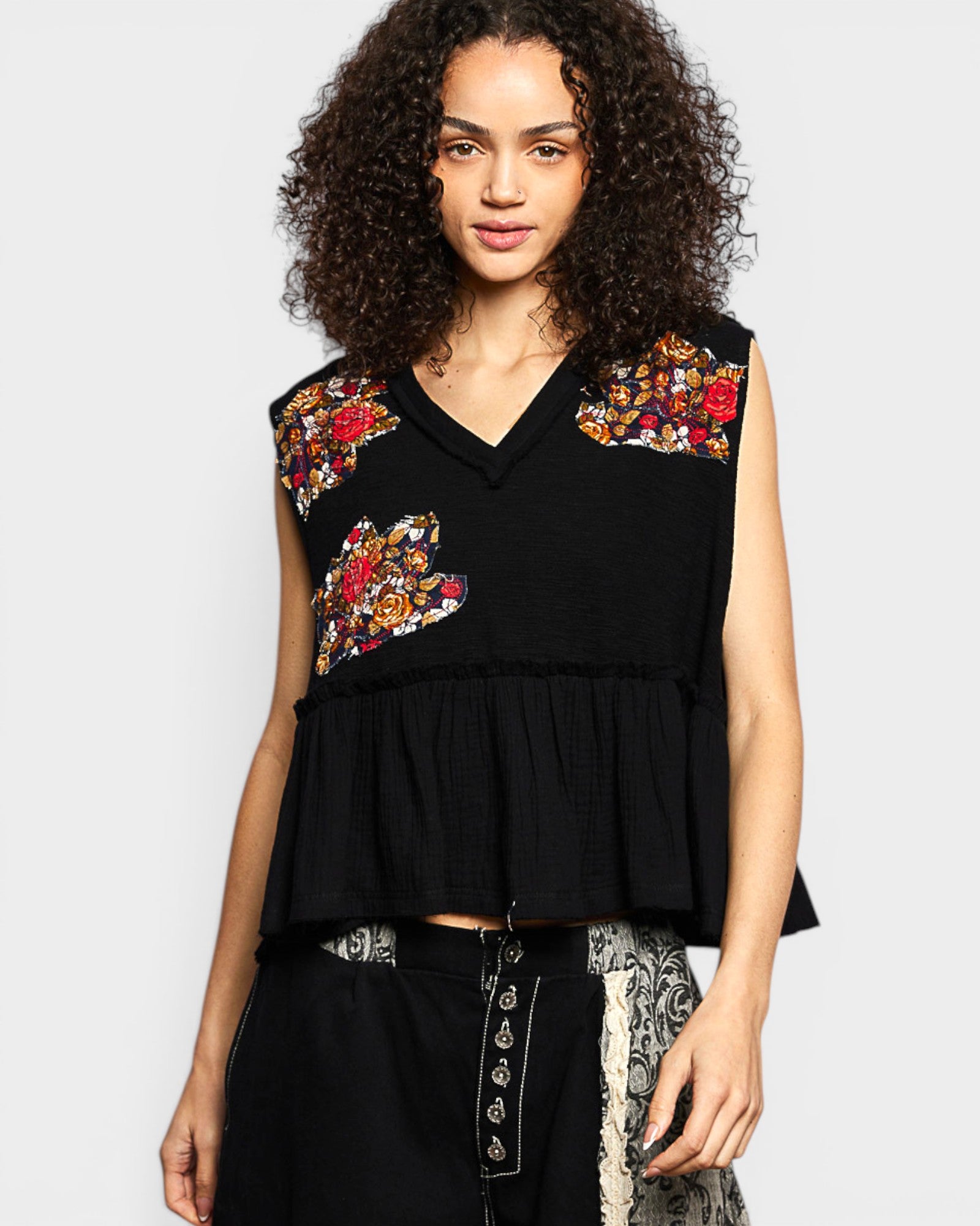 Woman wearing a black sleeveless top with floral embroidery on a plain background