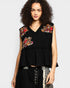 Woman wearing a black sleeveless top with floral embroidery on a plain background