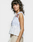 Woman wearing a white embroidered top against a plain background