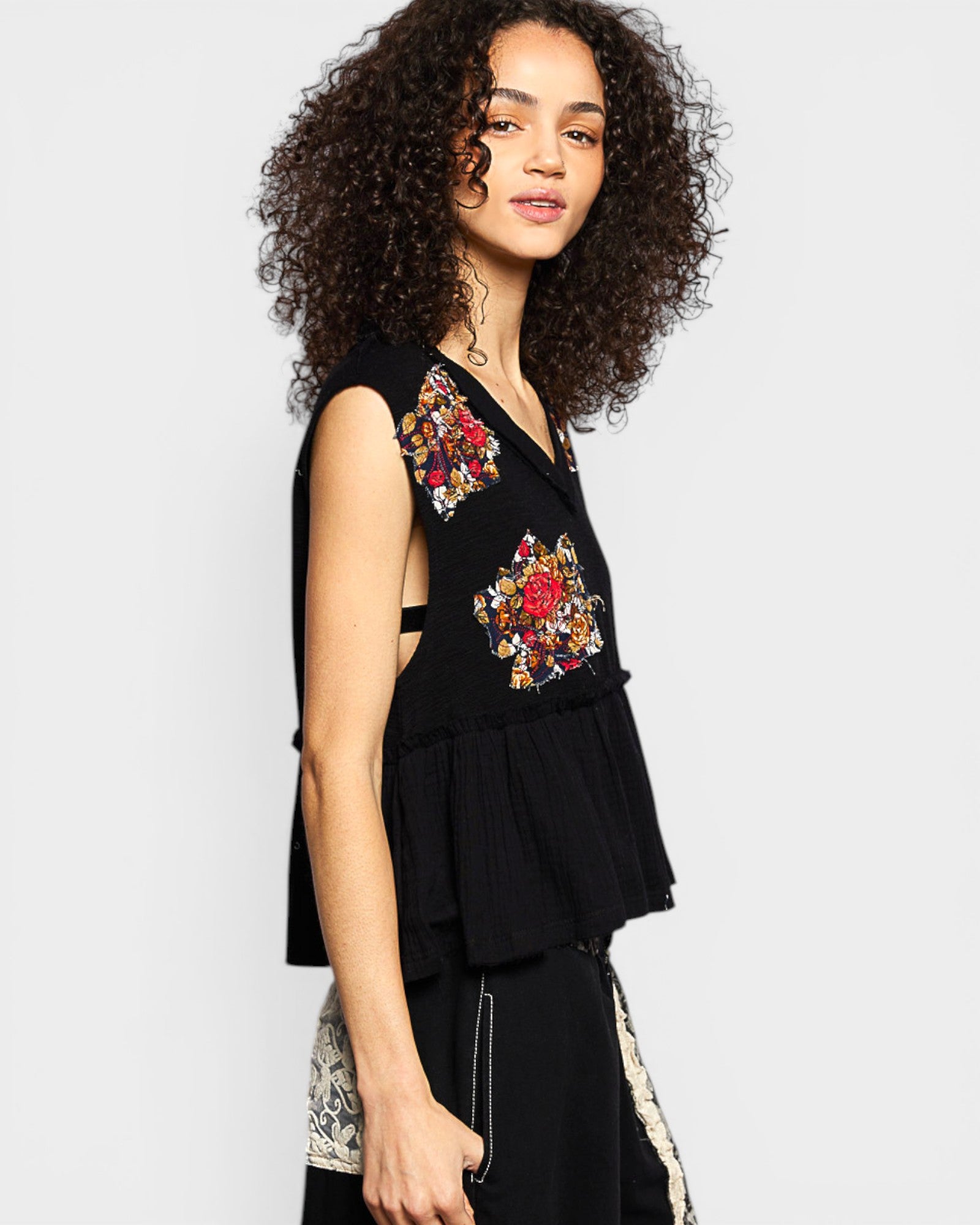 Woman wearing a black sleeveless top with floral embroidery on a light gray background