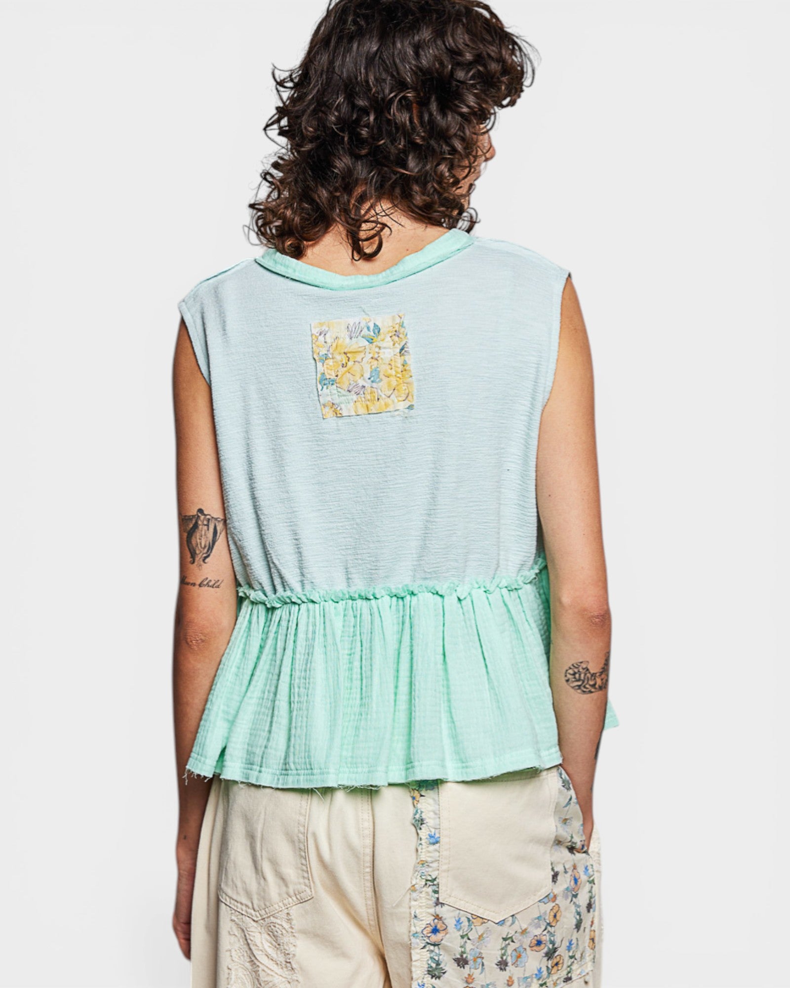 Person wearing a light blue sleeveless top with a floral pocket on a white background