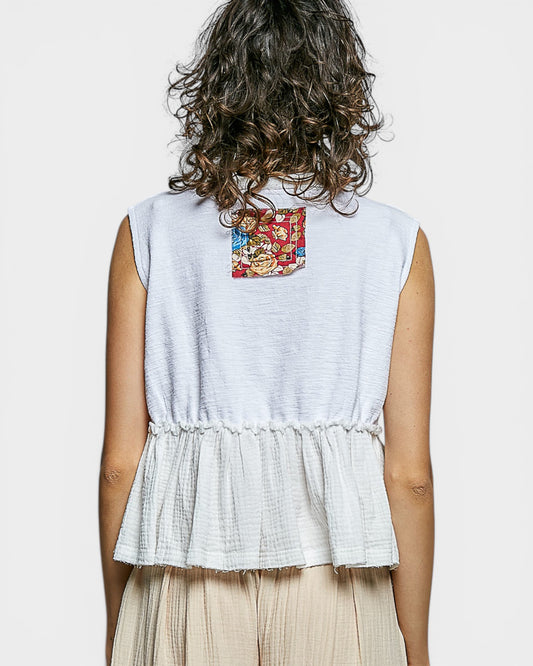 Person wearing a sleeveless white top with a colorful pattern on the back, standing against a plain background.