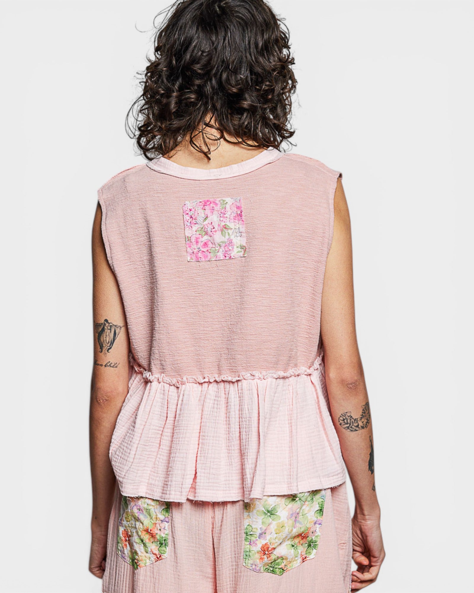 Person wearing a pink sleeveless top with floral patterns on a plain background