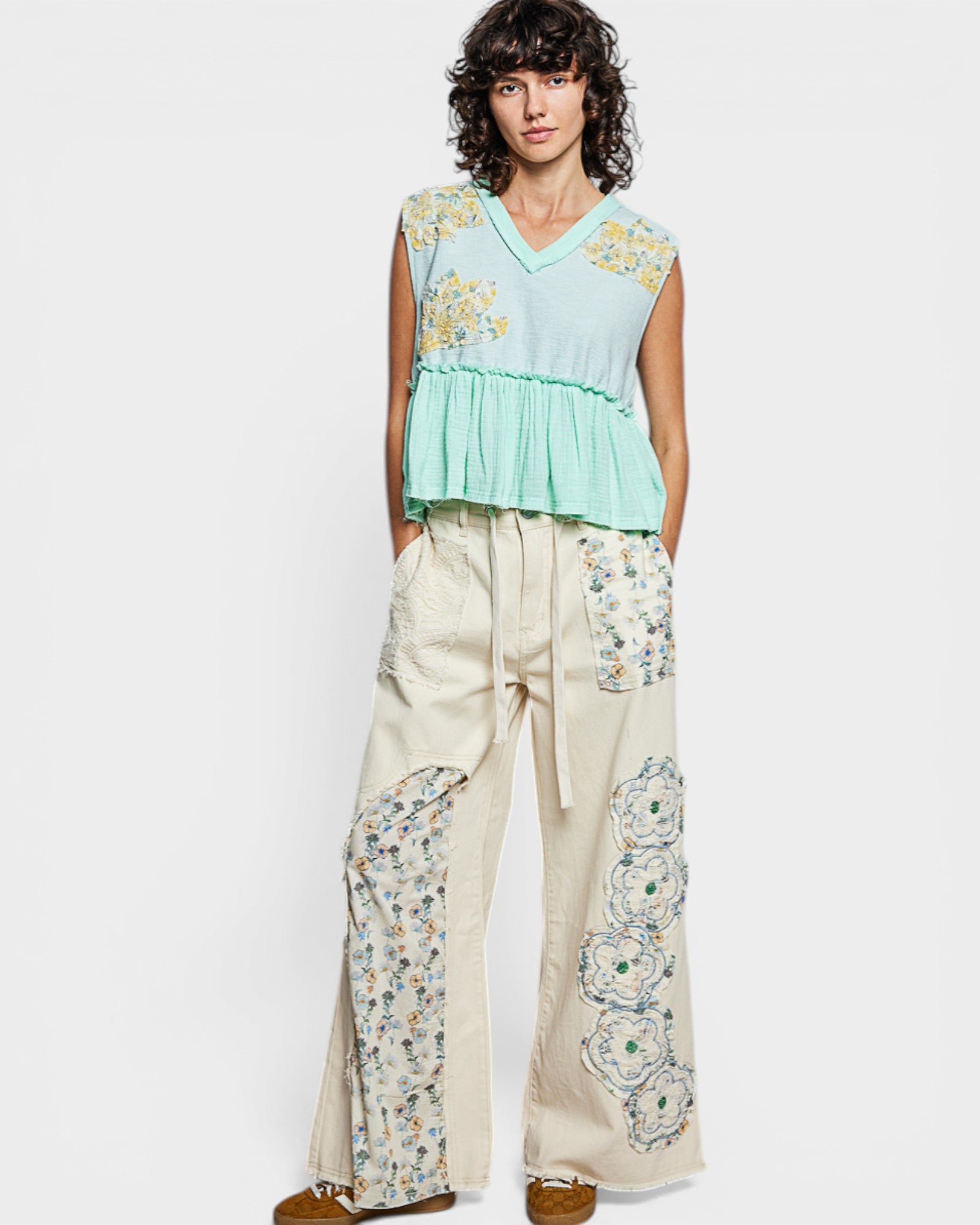 Woman wearing a light blue top and beige pants with floral patterns on a white background
