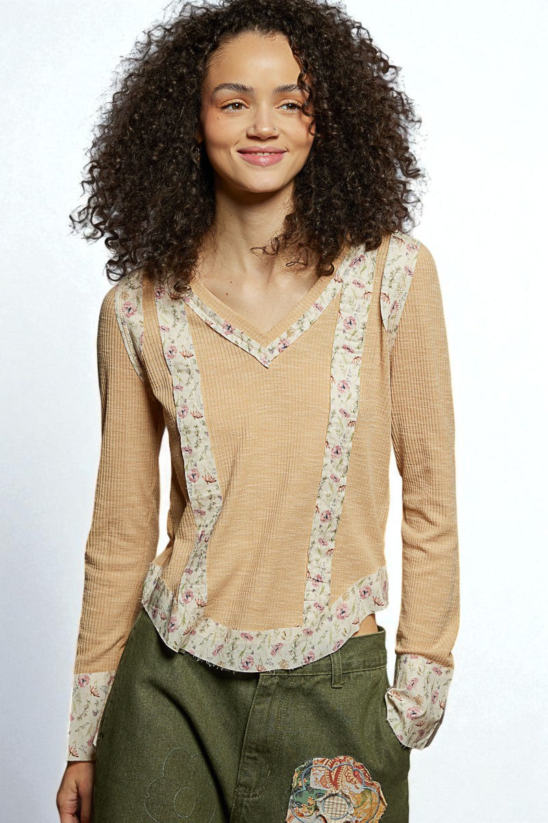Woman wearing a beige long-sleeve top with floral patterns on a plain background