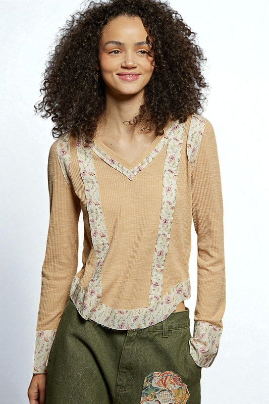 Woman wearing a beige long-sleeve top with floral patterns on a plain background