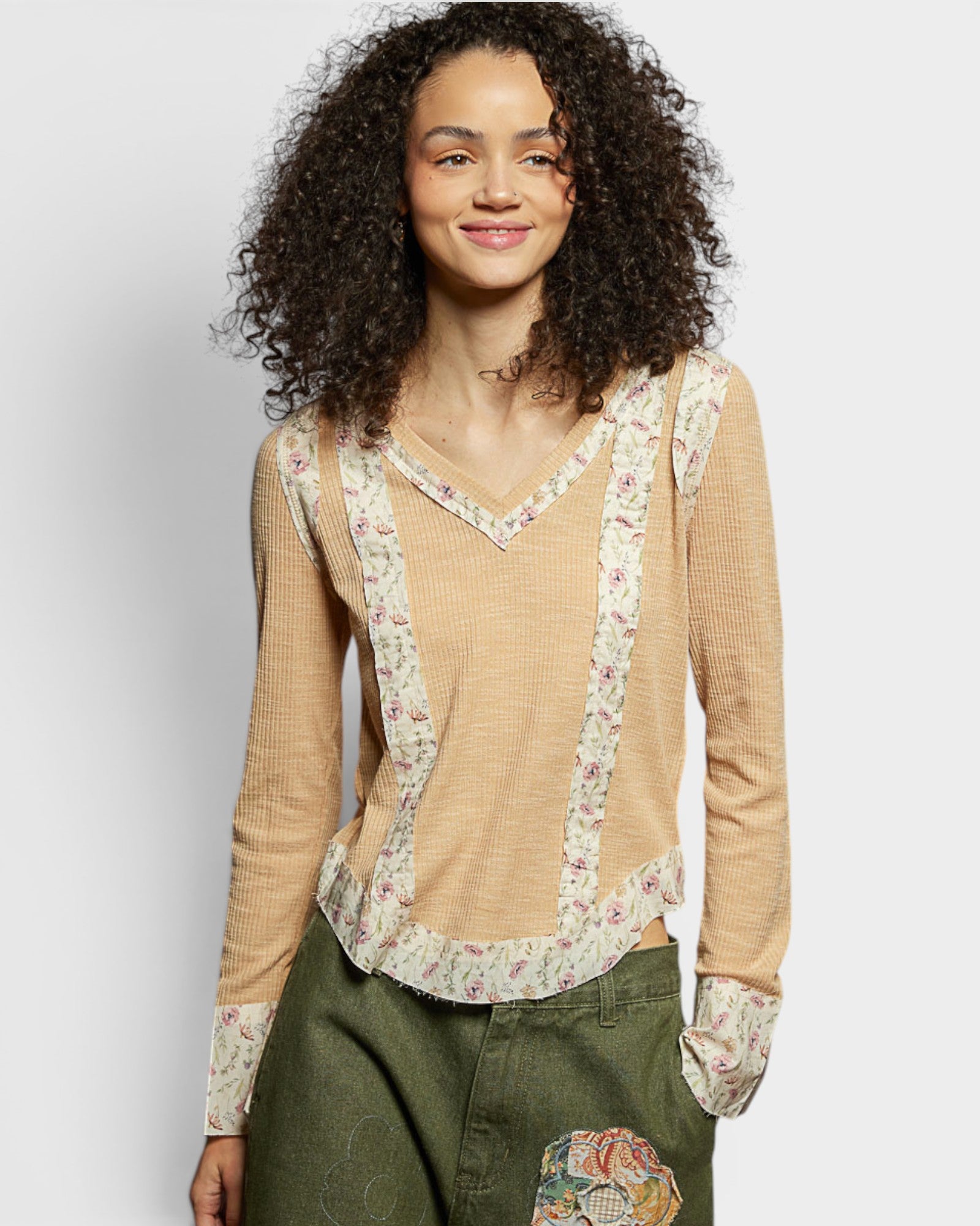 Woman wearing a beige long-sleeve top with floral details on a plain background