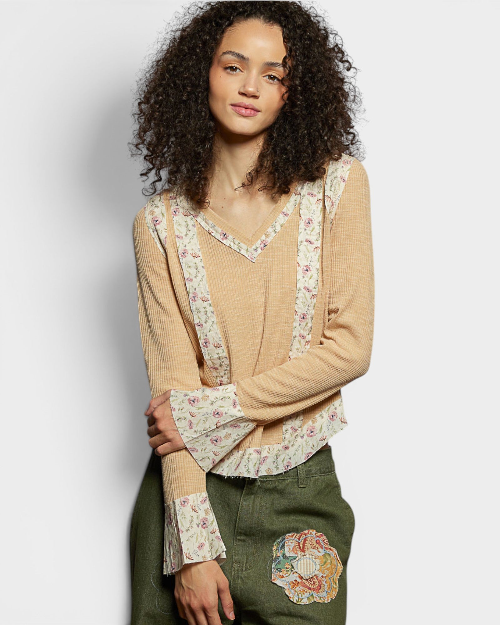 Woman wearing a beige sweater with floral patterns on a plain background