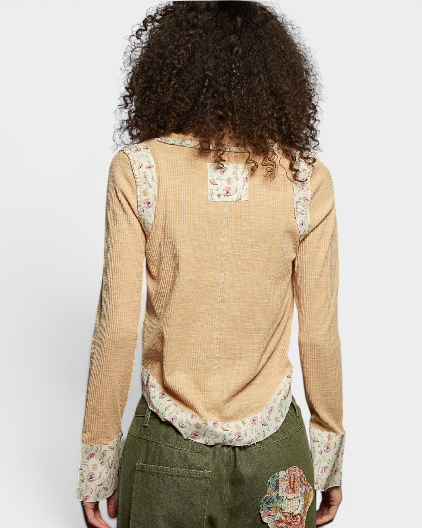 Woman wearing a beige blouse with floral patterns on a plain background