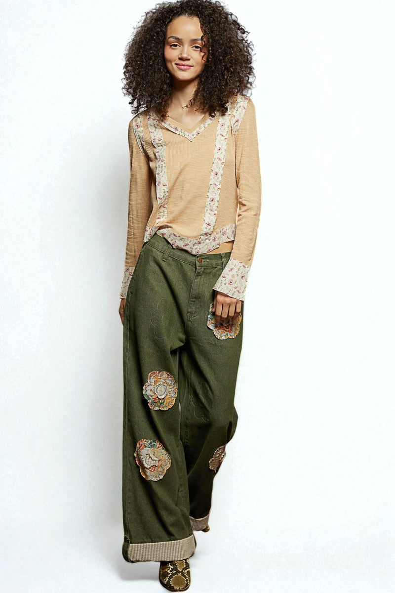 Woman wearing a beige top with floral patterns and green pants with floral patches on a white background