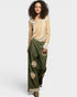 Woman wearing a beige top with lace details and green pants with floral patterns on a white background