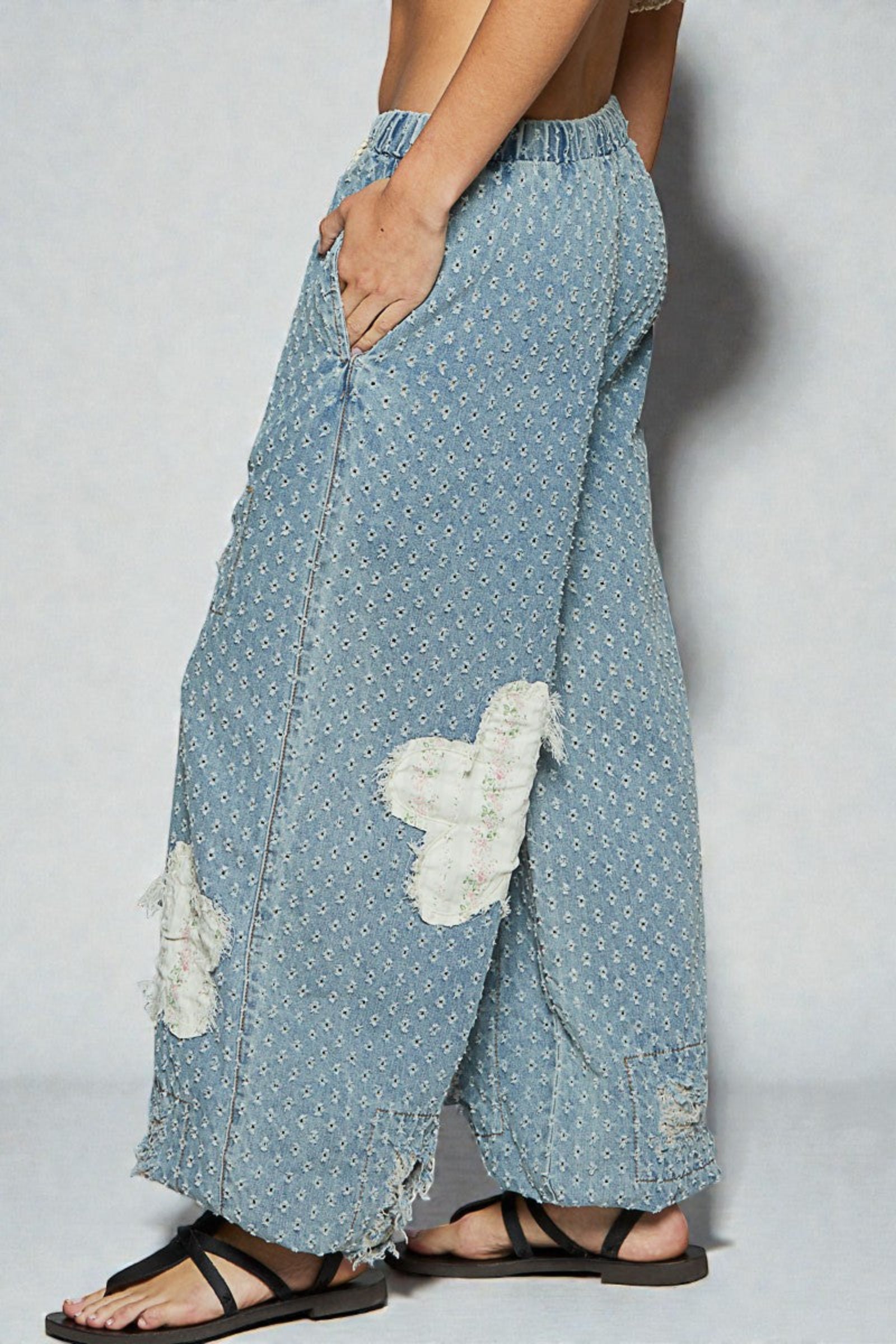 Light blue denim pants with white floral patches worn by a person on a plain background