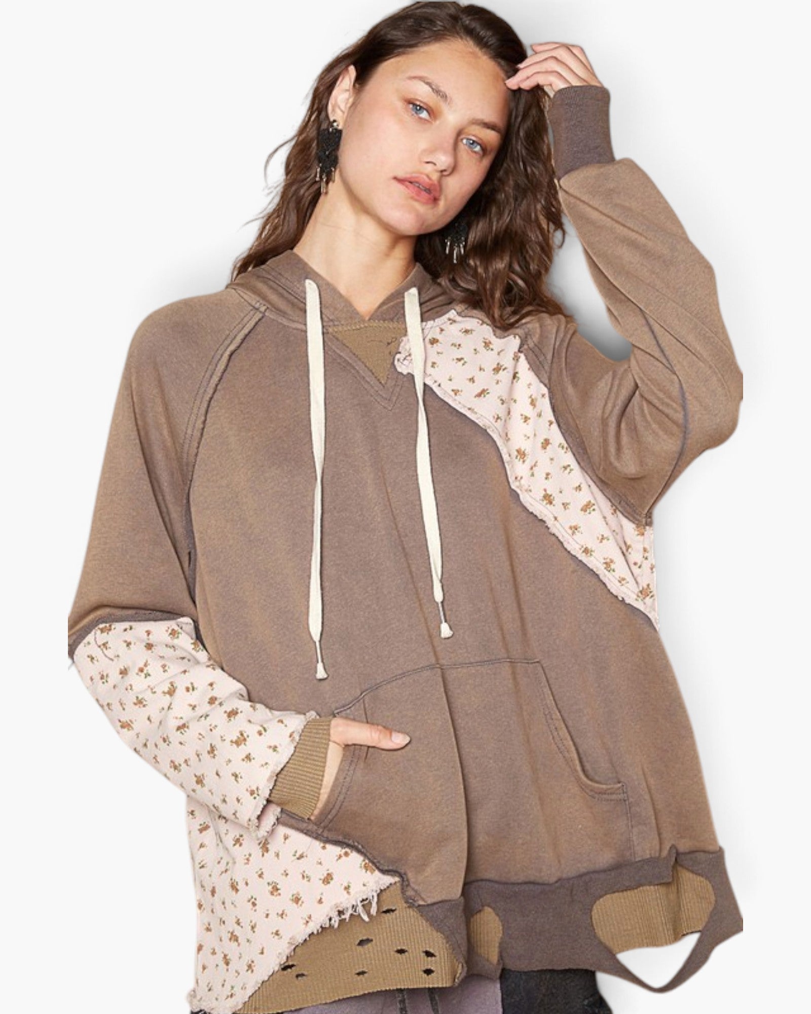 A woman modeling a brown hooded sweatshirt with beige patterned fabric panels on the sleeves and sides, white drawstrings, and a front kangaroo pocket, photographed against a plain light background.