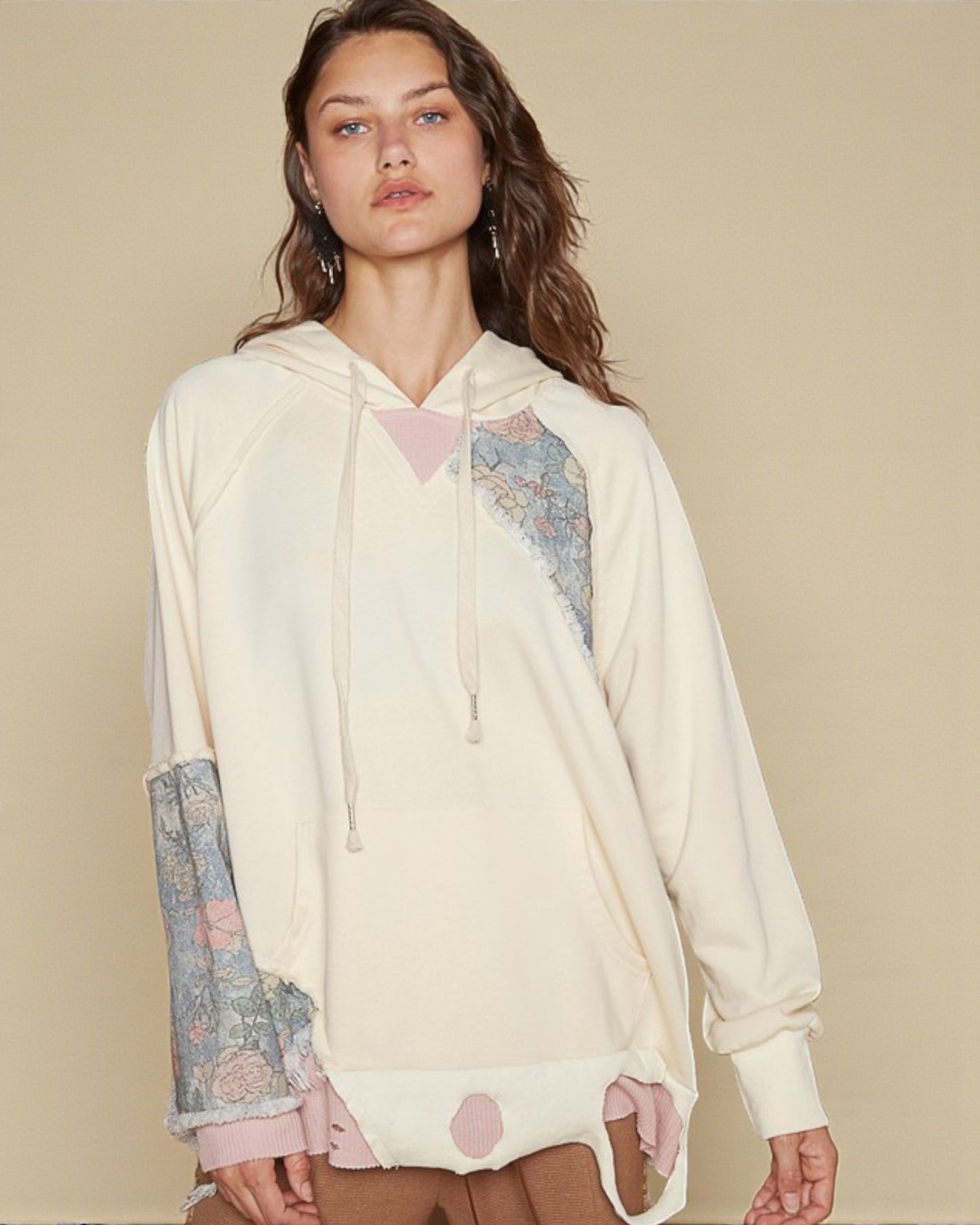 Woman wearing a cream-colored hoodie with floral patterned sleeves on a beige background