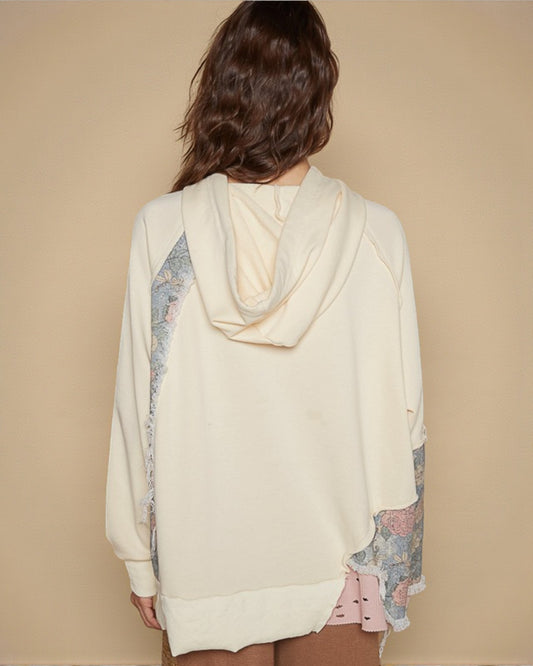 Person wearing a cream-colored hoodie with floral sleeves on a beige background