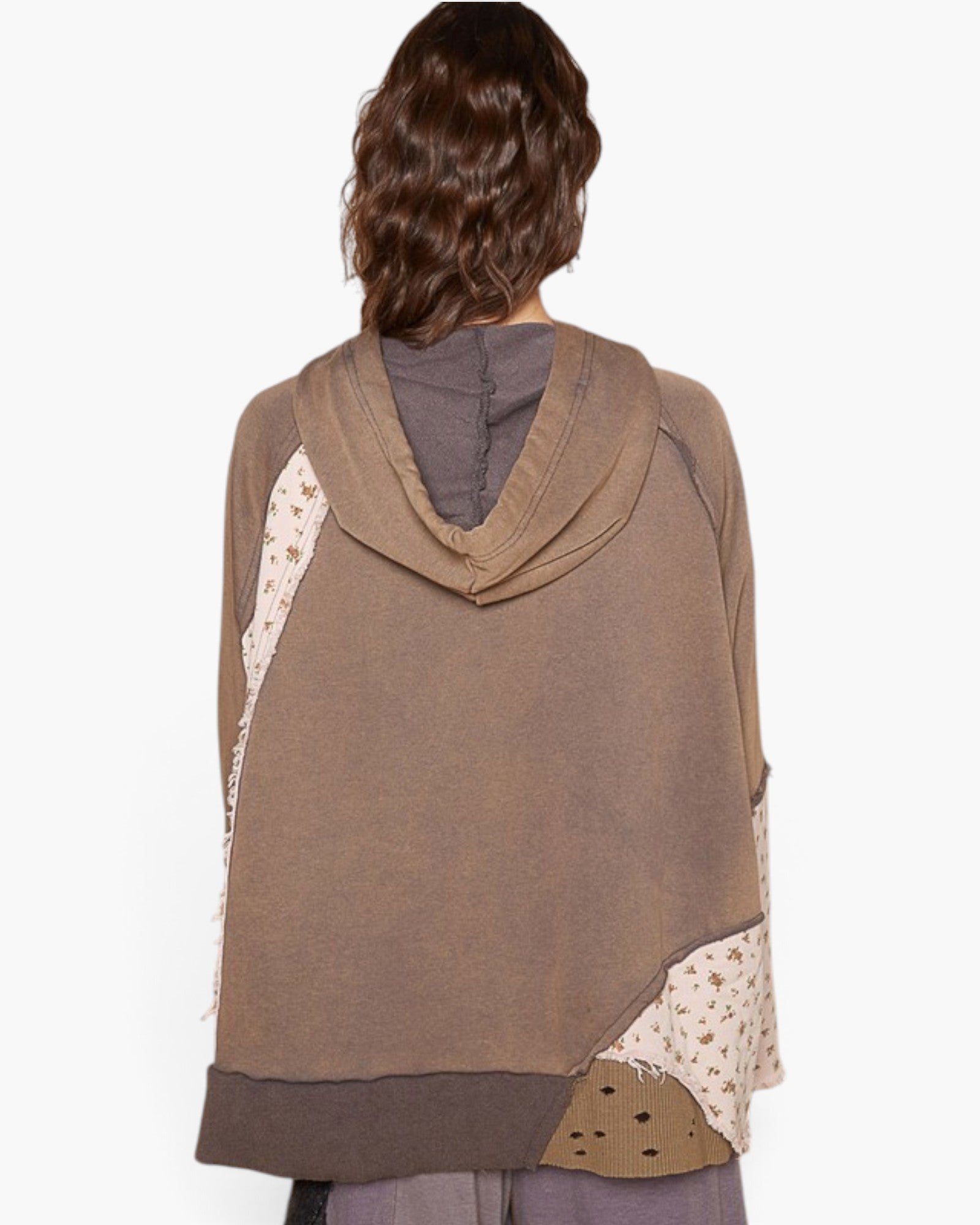 A person shown from the back wearing a brown patchwork poncho-style top with a cowl neck, solid brown base, and cream patterned side panels, against a plain light background.