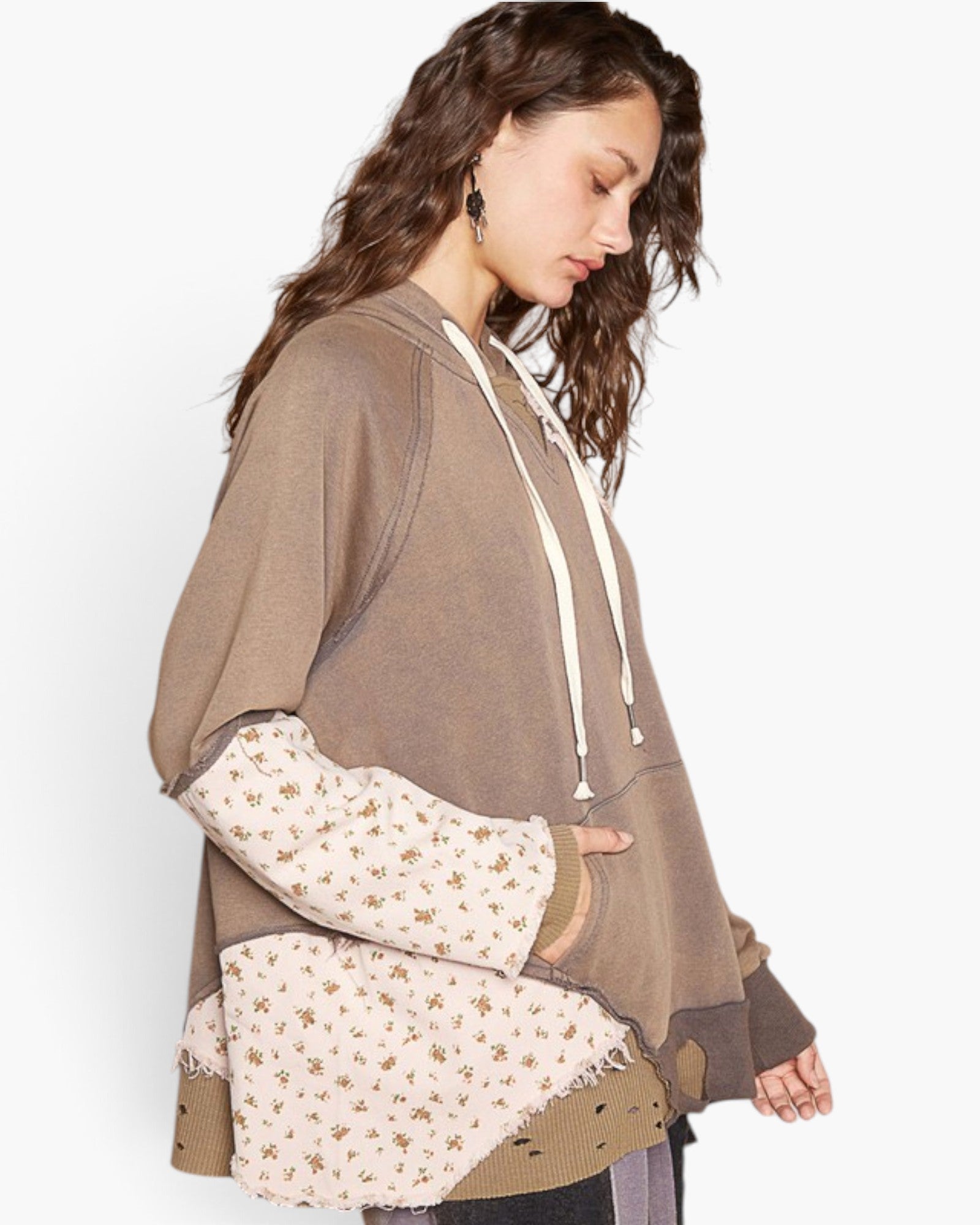 A woman wearing a brown patchwork hoodie with cream-colored drawstrings and patterned sleeves, shown from a side profile against a plain white background.