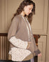 Woman wearing a brown hoodie with floral patterned sleeves against a beige wall.