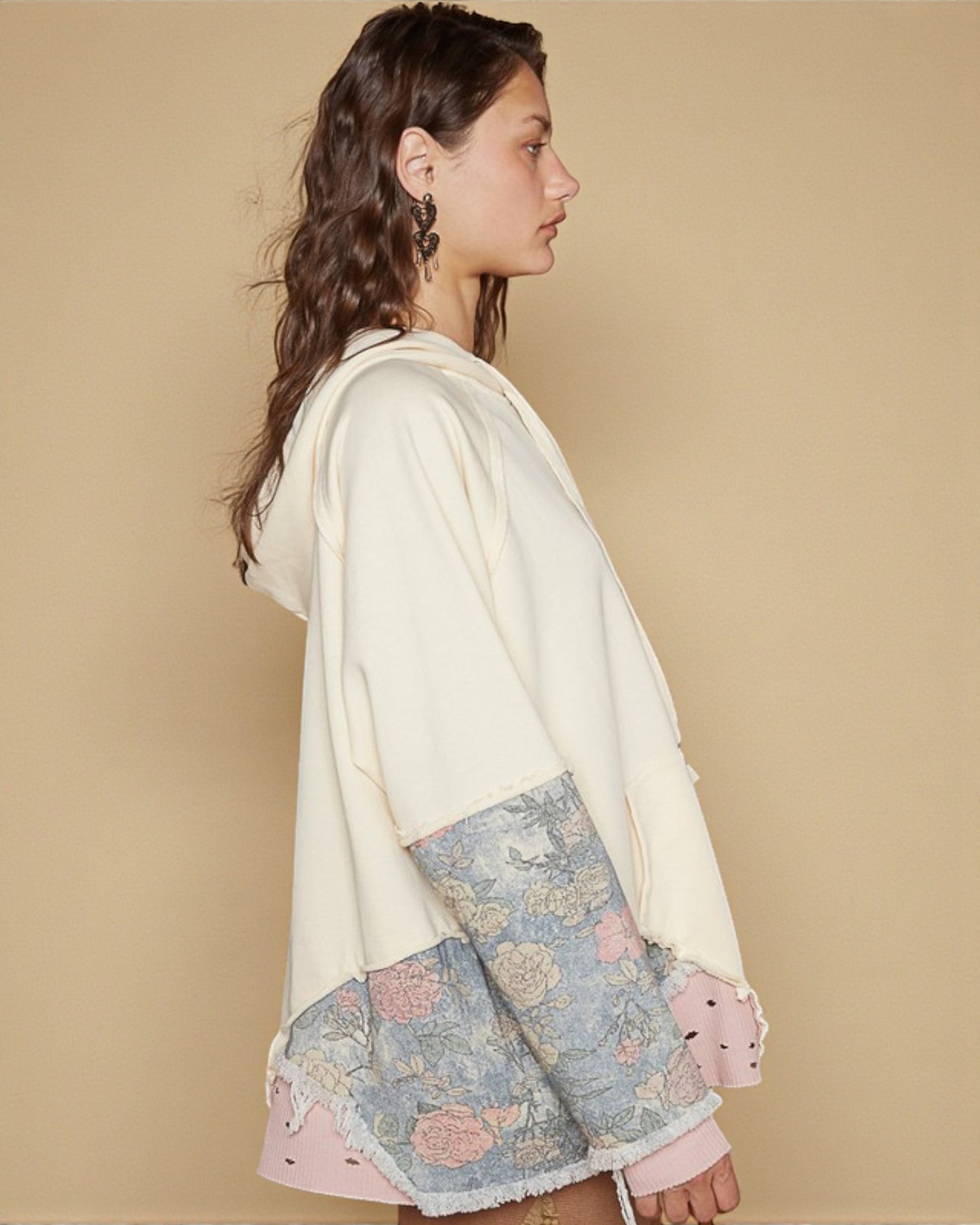 Woman wearing a cream hoodie with floral patterned sleeves against a beige background