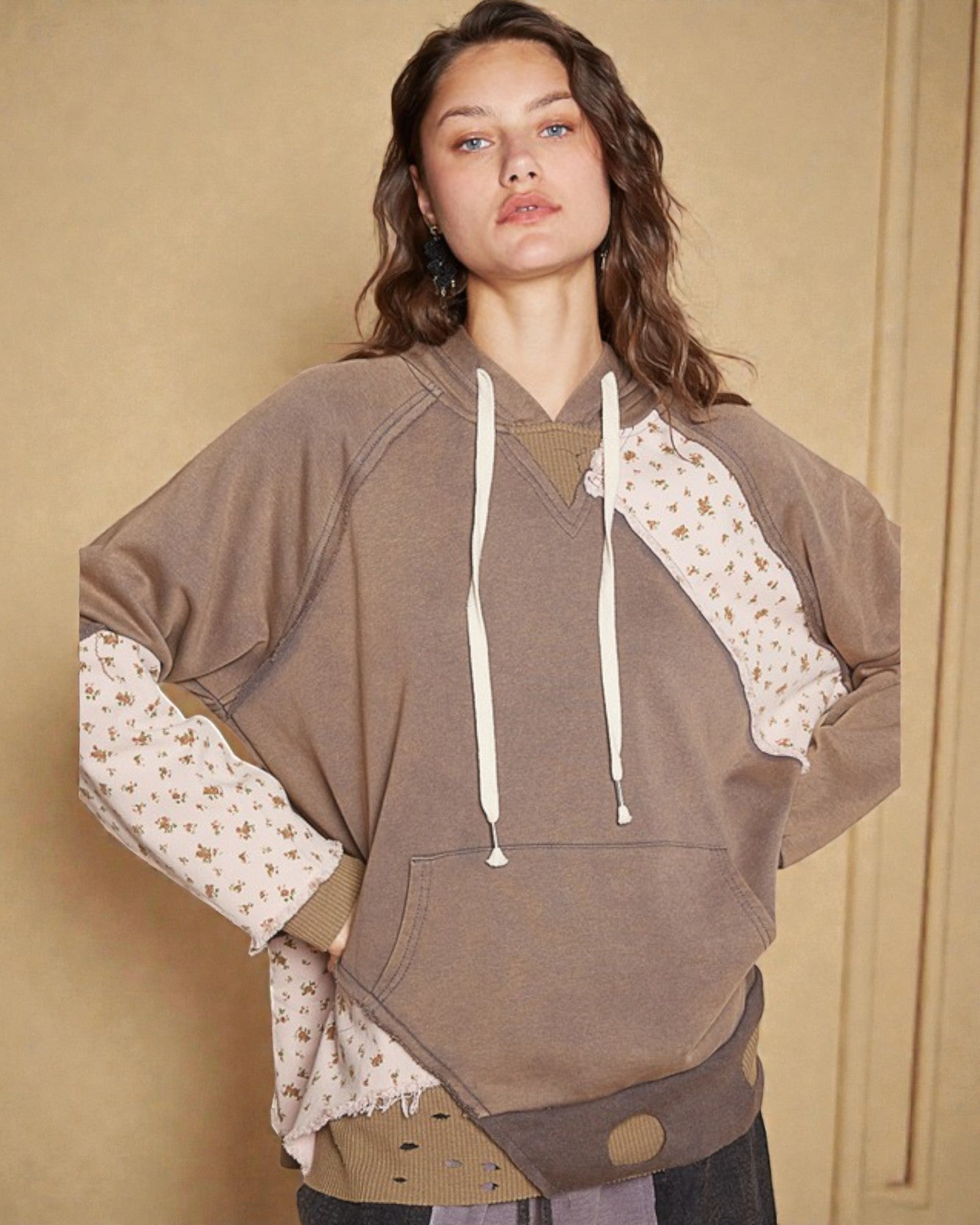 Woman wearing a brown hoodie with floral sleeves against a beige background