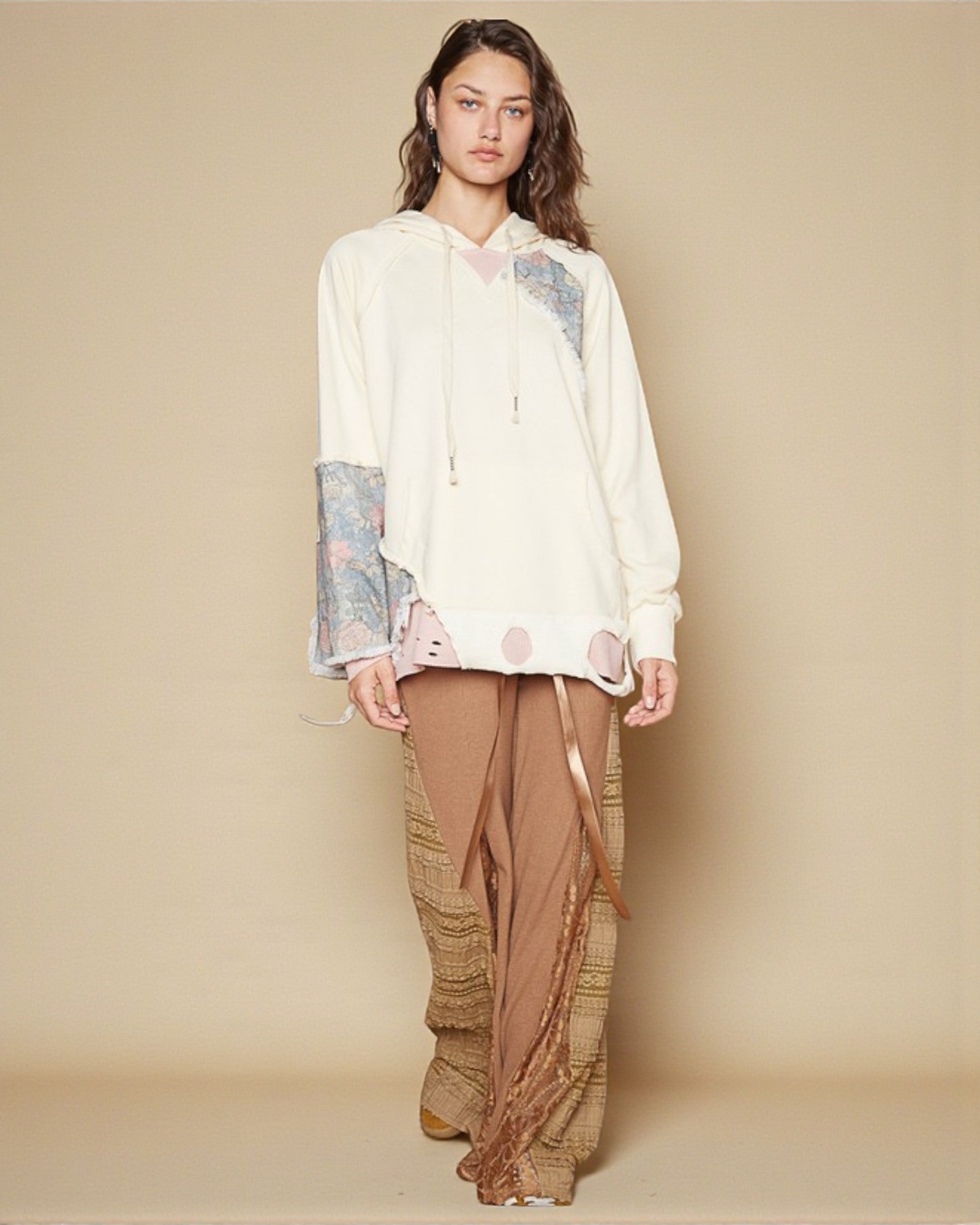 Woman wearing a white blouse with floral cuffs and brown patterned pants on a beige background