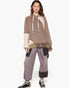 A model wearing a brown and beige patchwork hoodie with patterned sleeves, paired with matching wide-leg patchwork sweatpants and black sneakers, against a plain white background.