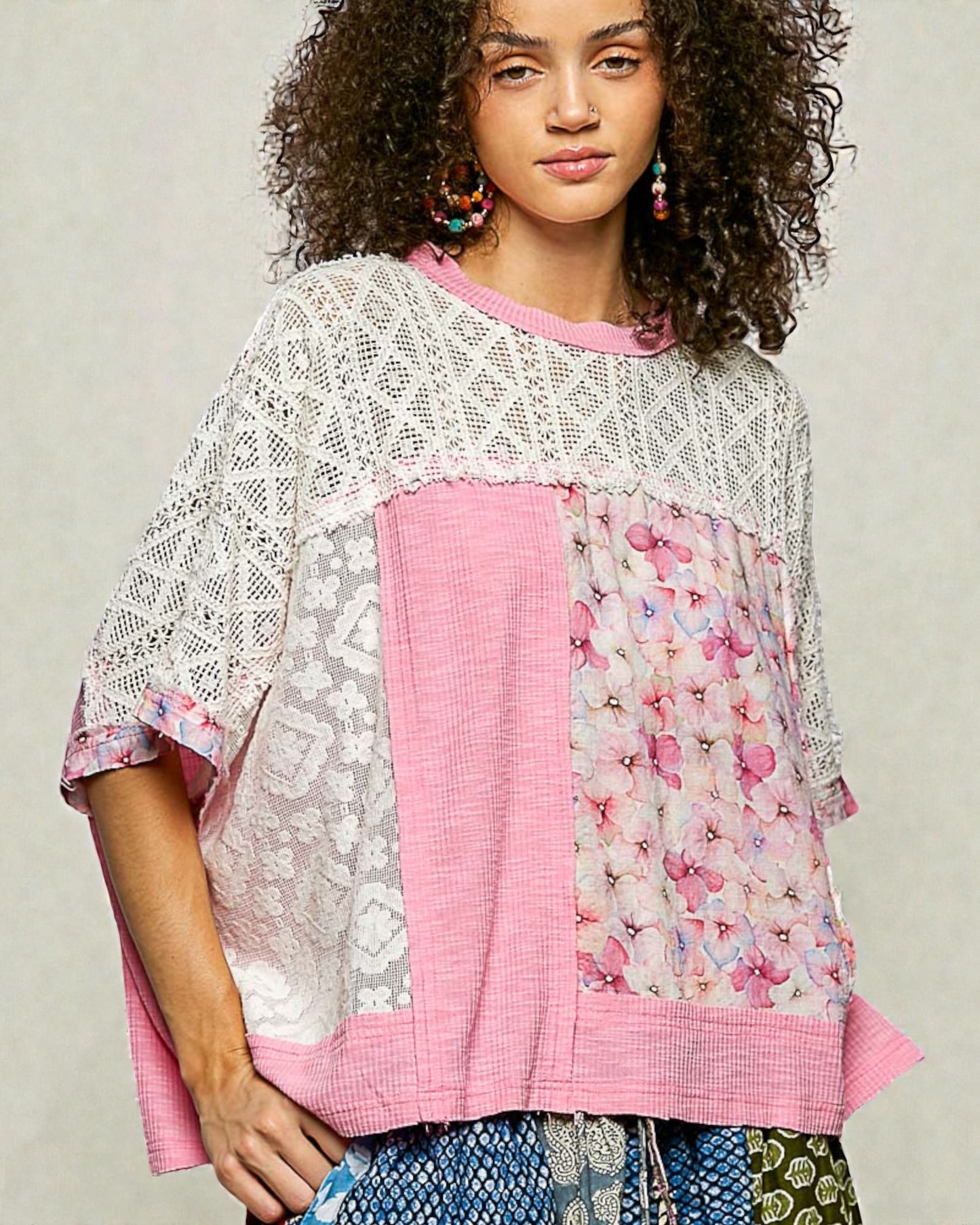 Woman wearing a colorful, layered top with floral and lace patterns on a neutral background