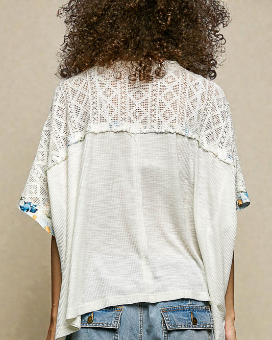 Person wearing a white lace top over a denim jacket on a beige background
