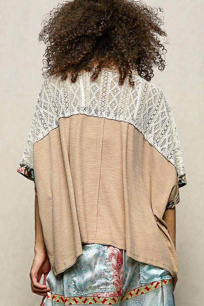 Person wearing a beige and white top with a textured pattern, standing against a plain background