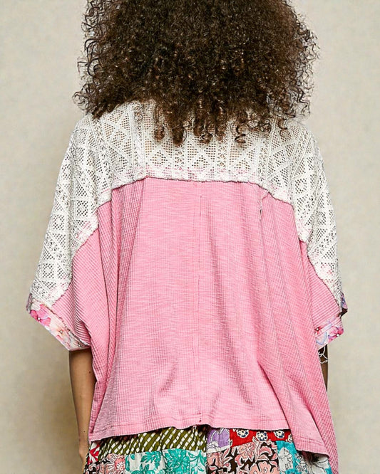 Person wearing a pink top with a white lace overlay against a neutral background