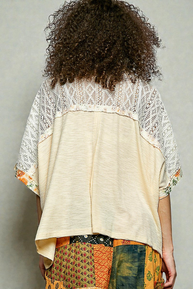 Person wearing a beige and white patterned top with colorful pants against a plain background