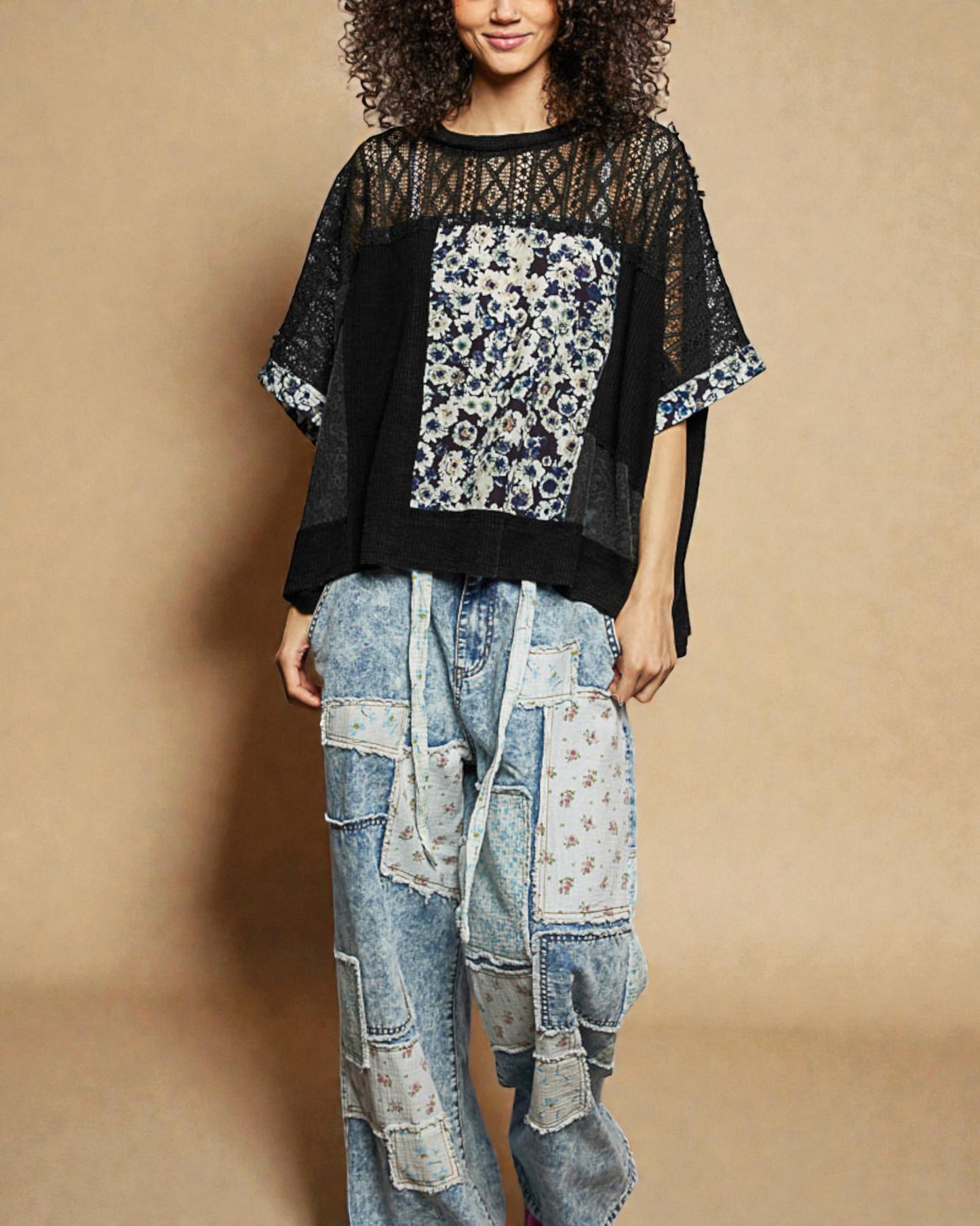 Person wearing a black sheer top with floral patterns and patchwork jeans on a beige background