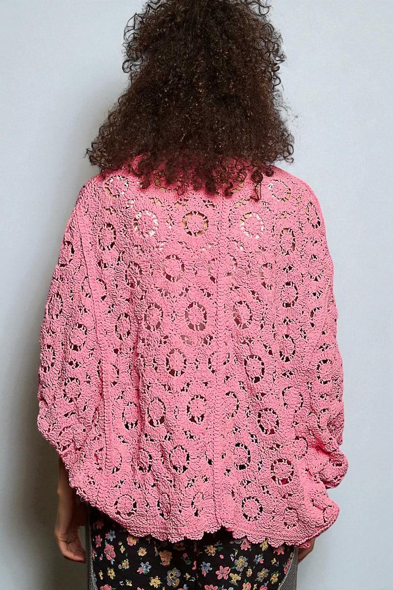 Person wearing a pink crochet sweater against a plain background