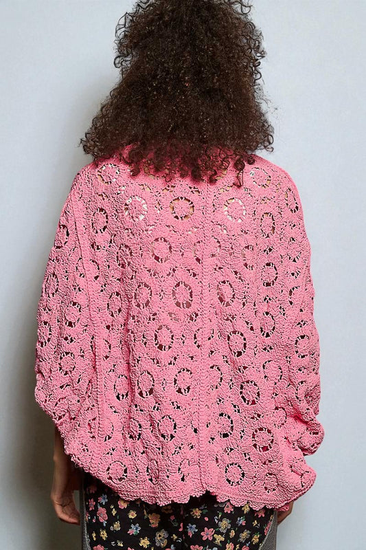 Person wearing a pink crochet sweater against a plain background